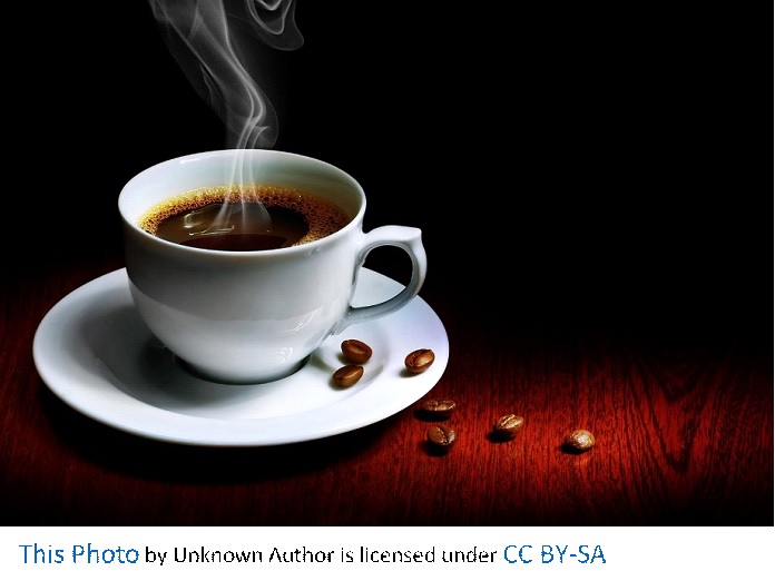 A steaming cup of black coffee is in a white mug on a white plate with coffee beans on the white plate and wood table.